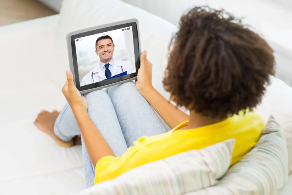 svg+xml;charset=utf em Maximídia - Seguro de Acidentes Pessoais e Seguro de Vida com o Máximo de Benefícios acidente pessoal: Paciente deita em uma cama e fala por videochamada em tablet com um médico, enquanto recebe atendimento à distância em ambiente doméstico.