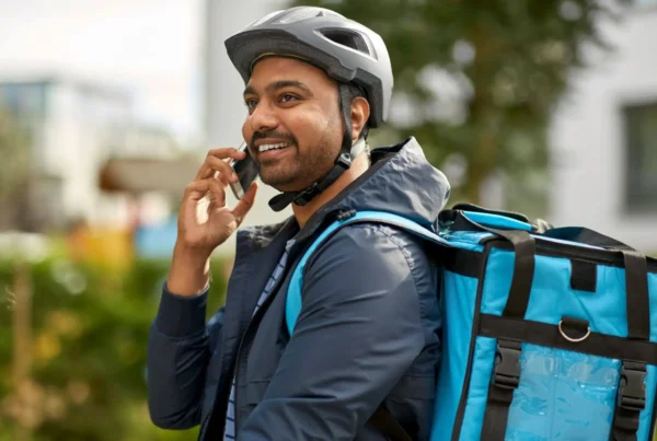 Homem com capacete e mochila azul falando ao celular ao ar livre, em ambiente urbano, sugerindo contratação de seguro acidente durante atividades diárias